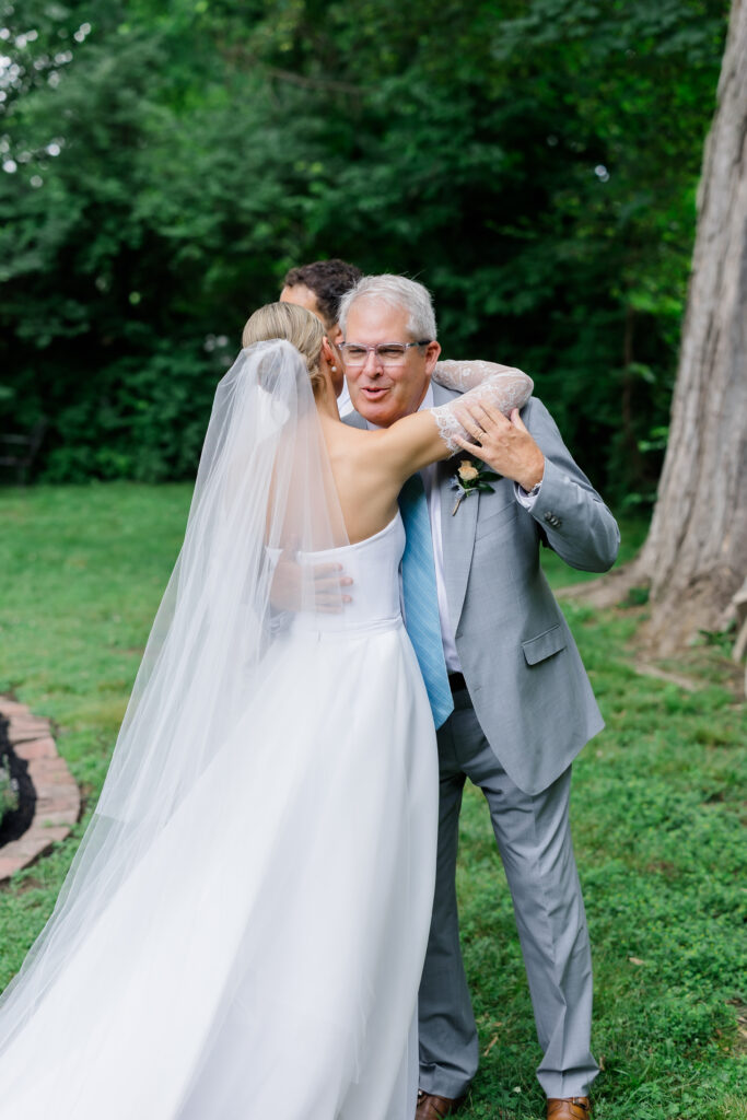 Bride’s father wiping tears during first look while brother smiles proudly beside them.