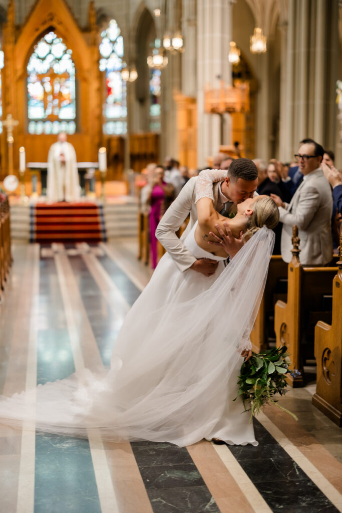 Bride and groom sharing first kiss in front of stained-glass altar at the Cathedral Basilica of the Assumption in Covington KY.