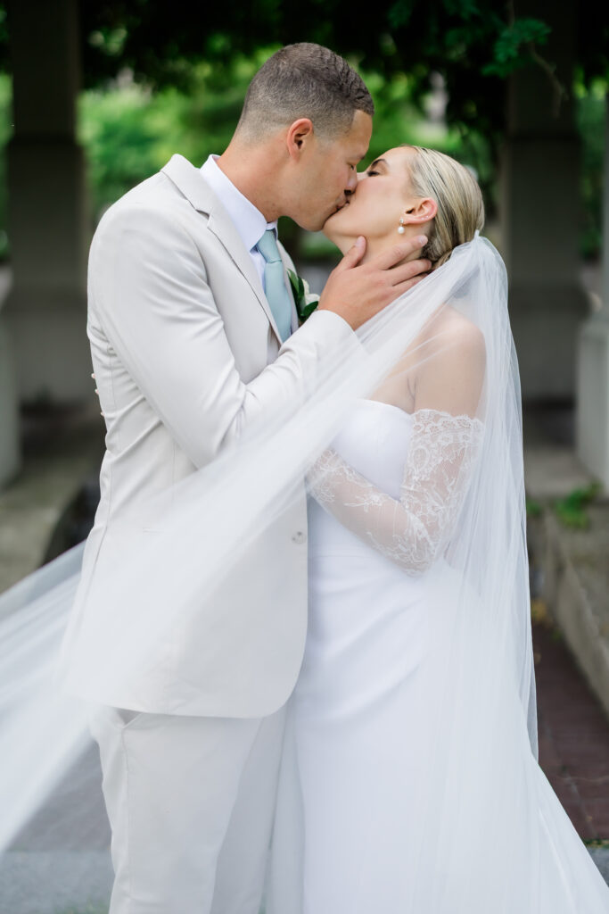Bride and groom sharing kiss under lush greenery arch in Covington KY garden.